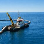 Tug with a yellow HEILA crane laying a floating pipeline at sea